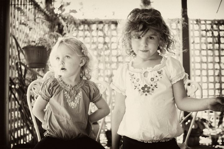 Two young children sitting on a sunlit verandah, looking toward the camera